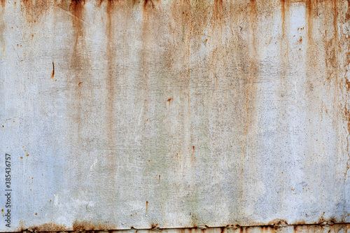The old metal wall is painted with white paint. Centers of corrosion and rust streaks are visible. Background. Texture.