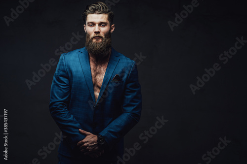 Bearded and mature businessman posing in blue suite with stylish haircut and serious face in dark background.