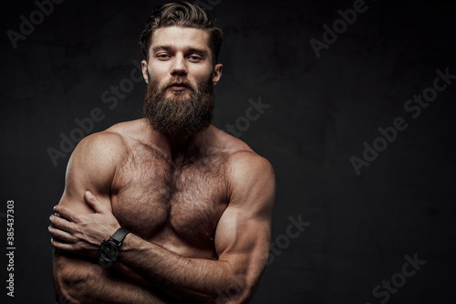 фотографія Naked man with muscular build and beard posing with crossed arms looking at camera in dark background