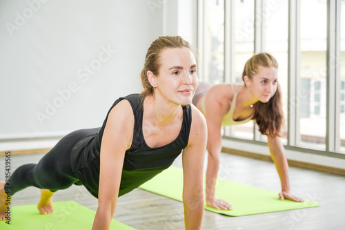 Couple of healthy young Caucasian women wearing sportswear with strength posture doing Yoga workout at home.