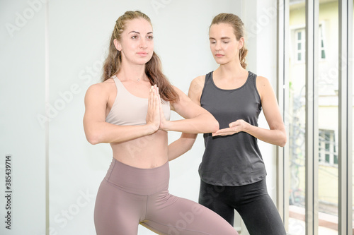 Couple of healthy young Caucasian women wearing sportswear with strength posture doing Yoga workout at home.