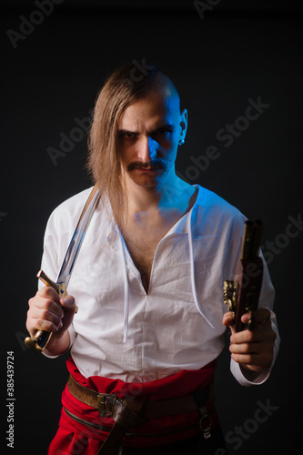 Kozak with weapons in national Ukrainian clothes. A young man with a forelock, in a white shirt and trousers with a red belt, holds a saber and a pistol. Warrior in battle photo