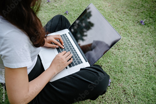 Beautiful Woman Relaxing and Using Laptop While Sitting on Grass Field, Asian Woman Working Online on Laptop Device and Joying .Social Media. Relaxation Leisure Activities Lifestyles/Work at Home