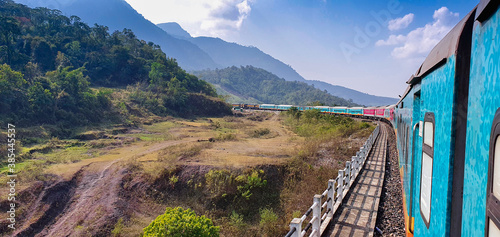 The beautiful multicolored train taking a turn on the mountainous terrain full of natural beauty and blue sky. Haflong, Assam, Northeast, India