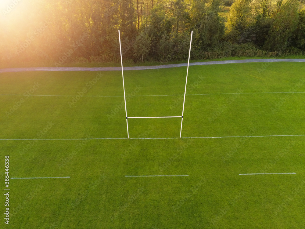 Fototapeta premium Aerial view on a green grass training pitch with tall goal posts at sunset, Field for popular Irish National sports: hurling, camogie, Gaelic football, rugby. Outdoors activity concept