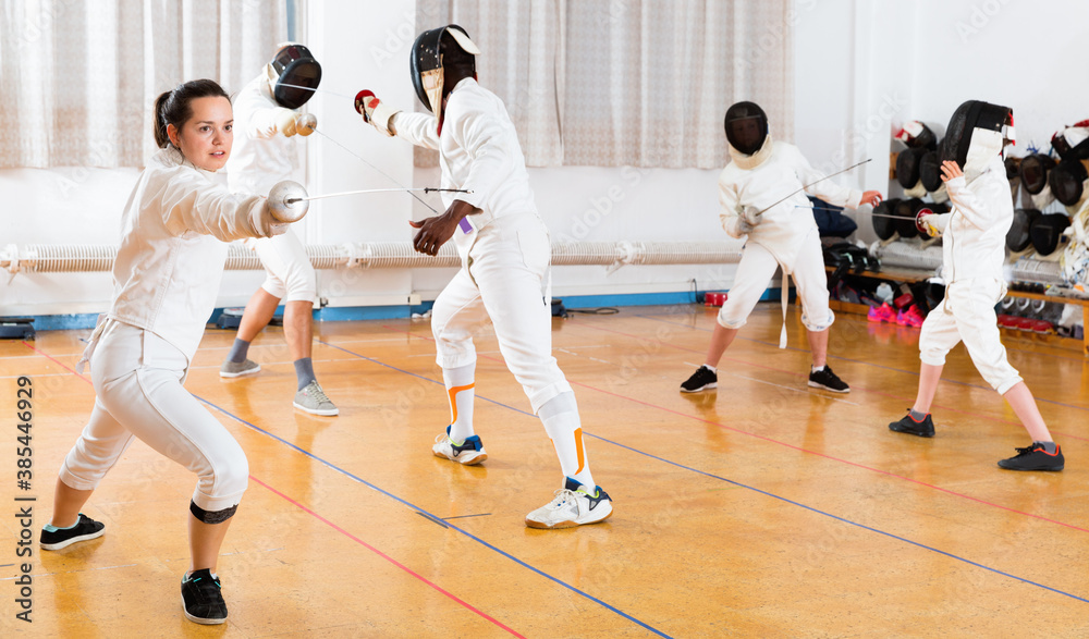 Young cheerful glad woman fencer practicing effective fencing techniques in training room