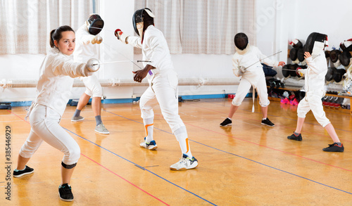 Young cheerful glad woman fencer practicing effective fencing techniques in training room