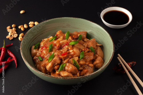 Kung Bao chicken on a black background. A Chinese dish with chicken, chili, peanuts, sauces and onions. photo