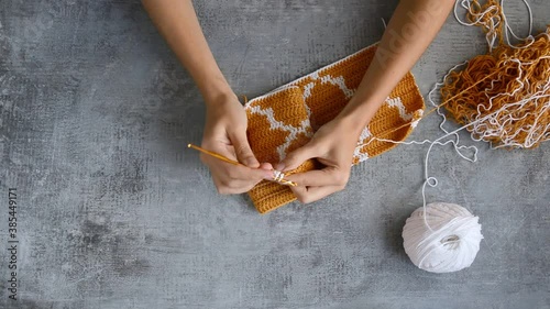 young womans hands crocheting with orange and white cotton thread on stone table background, top view close-up full HD stock video footage in real-time
