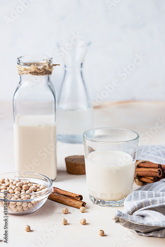Chickpea vegetarian milk in a bottle and glass and raw chickpeas on light stone background. Lactose free non dairy products. Healthy vegan food concept.