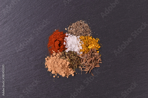 Salt pepper chilli curry oregano powders on black stone background

