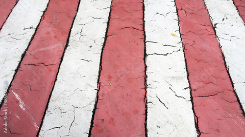 Top image, close - up of the pedestrian crossing marking. Top view of the texture of cracks on the asphalt. White and red stripes, diagonal, vertical, perspective. Flat layout.