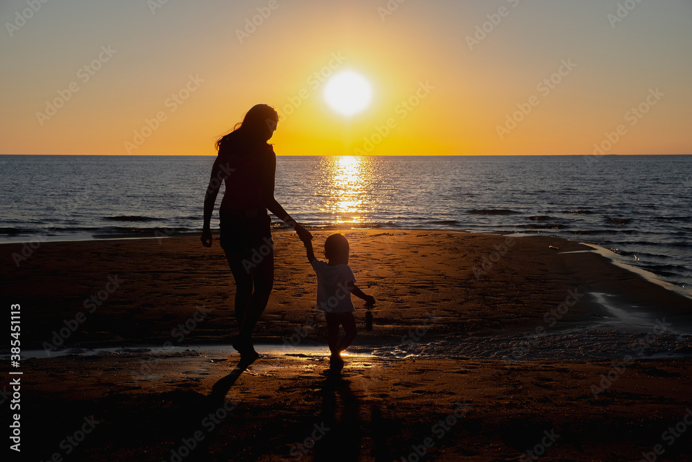 Mother and son are walking on the beach near the sea and admiring beautifil sunset. Happy family concept. Holiday concept. Happy family vacation. Family fun.