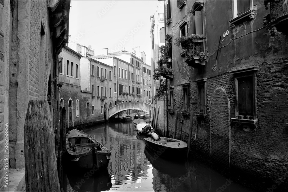 Venice, Italy, December 28, 2018 evocative black and white image of a typical Venice canal with moored boats and connecting bridges
