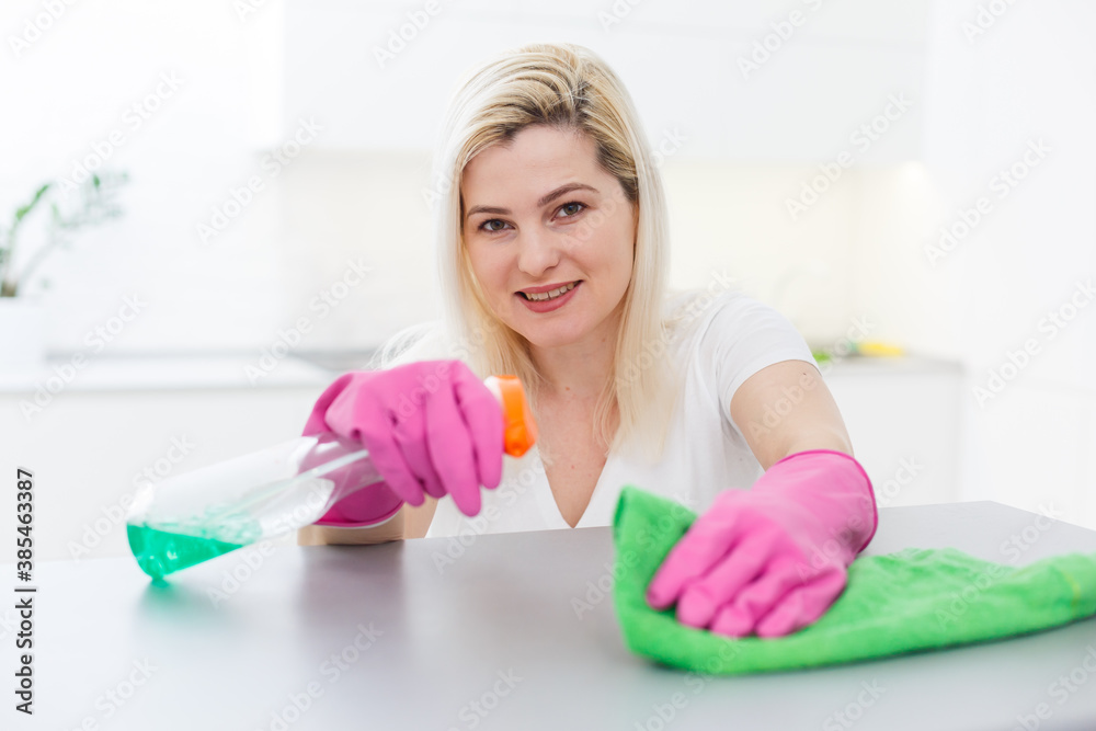 Cleanness is in trend. Pretty smiling woman wiping table with cloth and special means of washing Cleanness is in trend. Pretty smiling woman wiping table with cloth and special means of washing