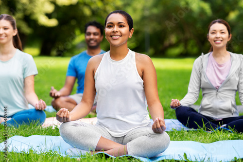 fitness, sport, yoga and healthy lifestyle concept - group of happy people meditating in lotus pose at summer park
