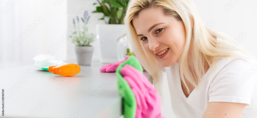 Woman in protective gloves is smiling and wiping dust using a spray and a duster while cleaning her house, close-up Woman in protective gloves is smiling and wiping dust using a spray and a duster while cleaning her house, close-up