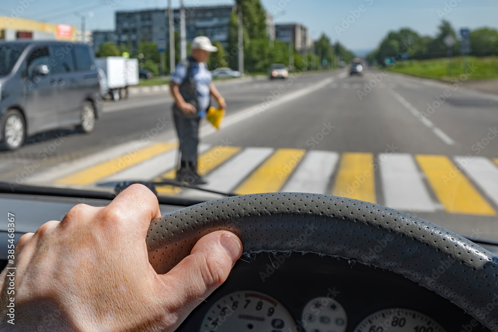 driver hand on the steering wheel of a car against the background of a pedestrian passing through a Zebra crossing