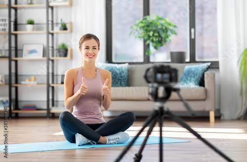 fitness, sport and video blogging concept - woman or blogger with camera on tripod recording online training class at home