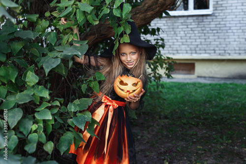 Little girl in witch costume on Halloween trick or treat in garden