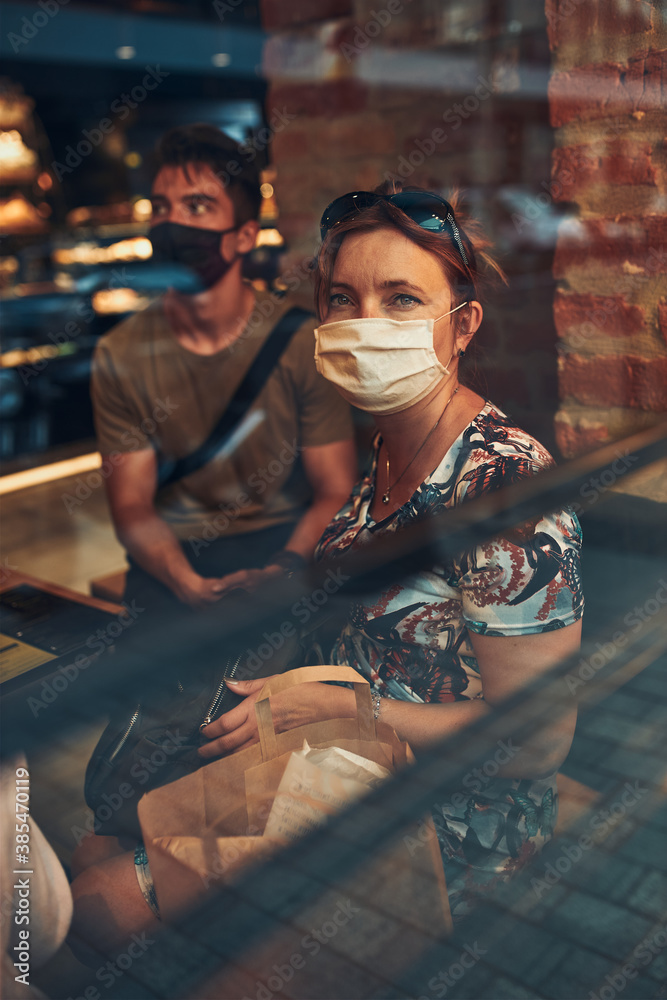 Family sitting in coffee shop at store front in the city center in the evening, wearing the face mask to avoid virus infection and to prevent the spread of disease in time of coronavirus