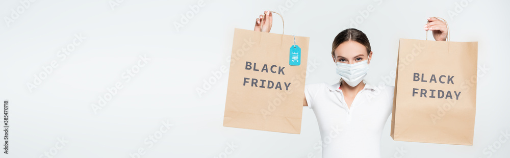 panoramic shot of customer in medical mask holding shopping bags with sale tag and black friday lettering isolated on white panoramic shot of customer in medical mask holding shopping bags with sale tag and black friday lettering isolated on white