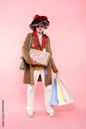 young woman in sunglasses and hats with sale tags holding box with favorite shoes lettering and shopping bags on pink, black friday concept