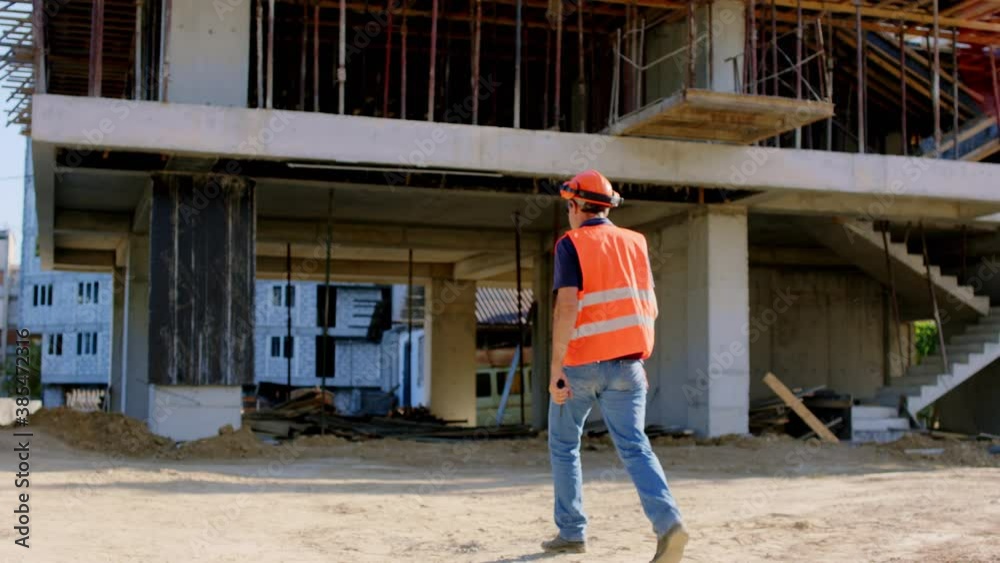 At big construction site walking foreman in a safety equipment to the construction site taking video from the back At big construction site walking foreman in a safety equipment to the construction site taking video from the back