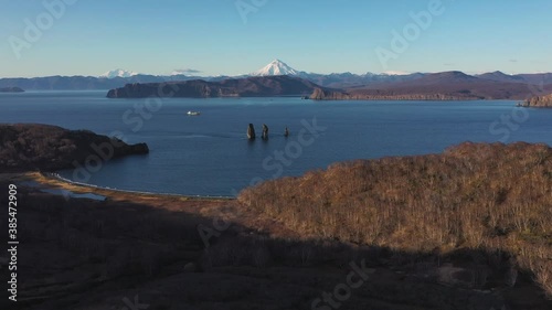 Autumn scenery, beautiful sunrise over Avacha Bay on Russia's Kamchatka Peninsula, and the famous Three Brothers Rock. The waters of the Pacific Ocean. In the background is the Avachinsky volcano.