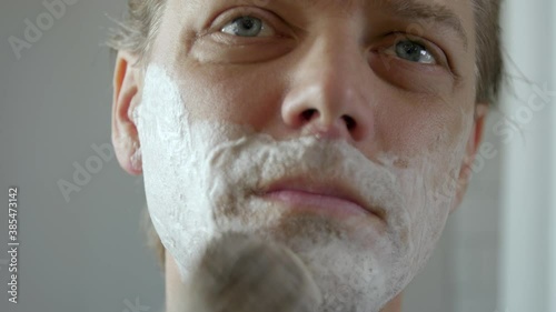 A blonde haired man shaves off a scraggily beard with a safety razor after quarantine. photo