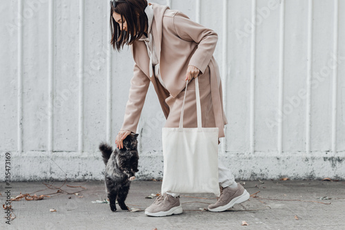 Woman in coat with white cotton bag in her hands and cute cat sitting near. Mockup and zero waste concept. photo