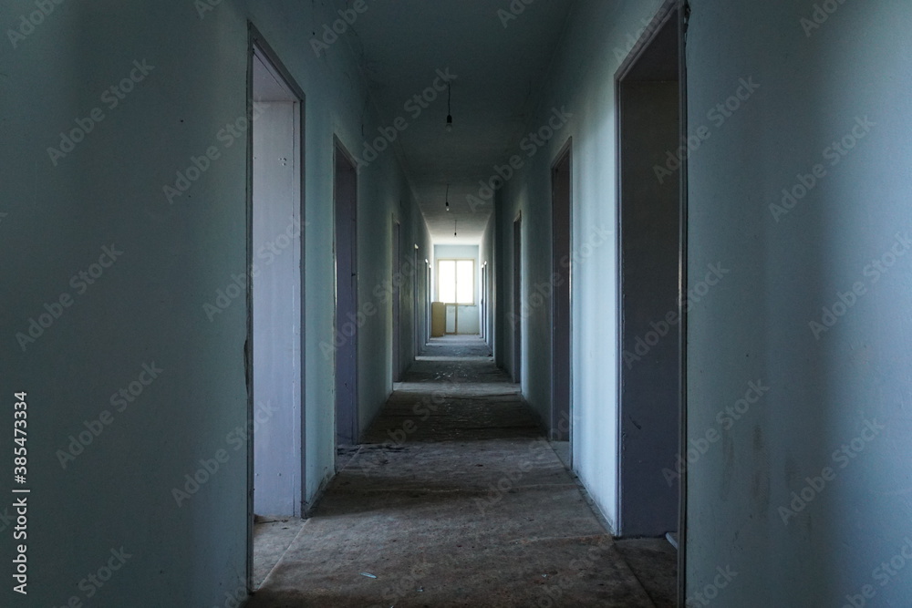 Corridor with blue walls, many doors and a bright light window at the bottom, part of an abandoned building