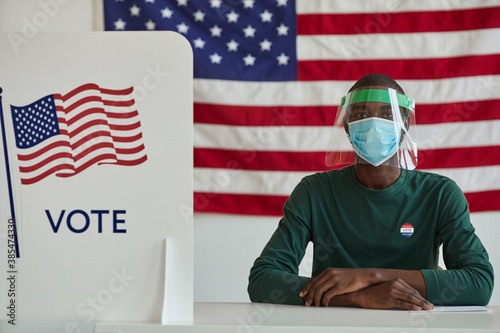 Portrait of African man in protective mask sitting at the table and working in voting at American polling station