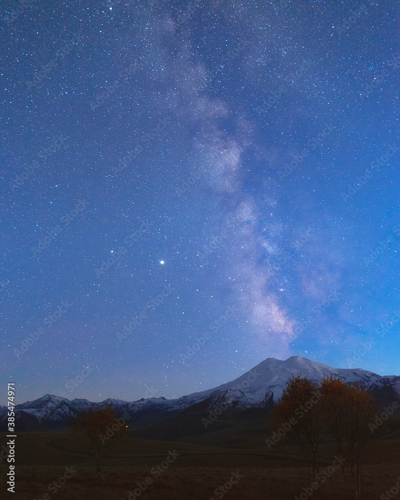 Milky Way in the blue evening sky over the snow-white summit of Mount Elbrus