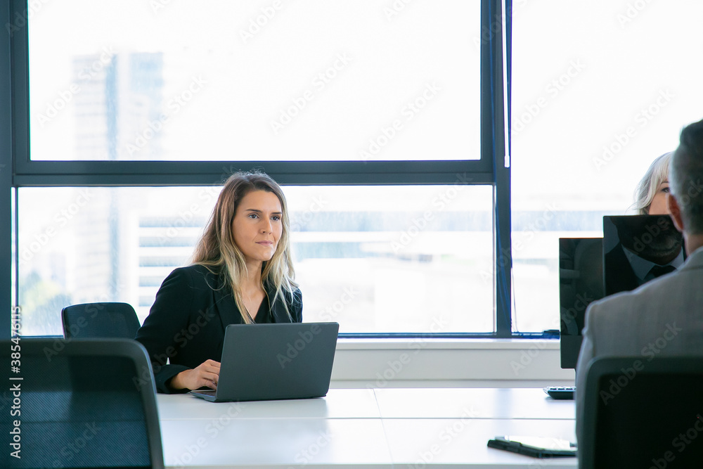Young manager sitting at table and working via laptop. Beautiful pensive businesswomen thinking about work and looking away. Cropped colleagues working with computers. Business and occupation concept Young manager sitting at table and working via laptop. Beautiful pensive businesswomen thinking about work and looking away. Cropped colleagues working with computers. Business and occupation concept