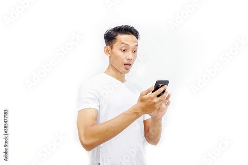 Young asian man holding smartphone and surprised by notification on his smartphone about discount or cash back from online shop. Millennial and business concept.  © Habib