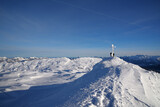 Zwei Winterwanderer auf einem verschneiten Gipfel mit einem Gipfelkreuz