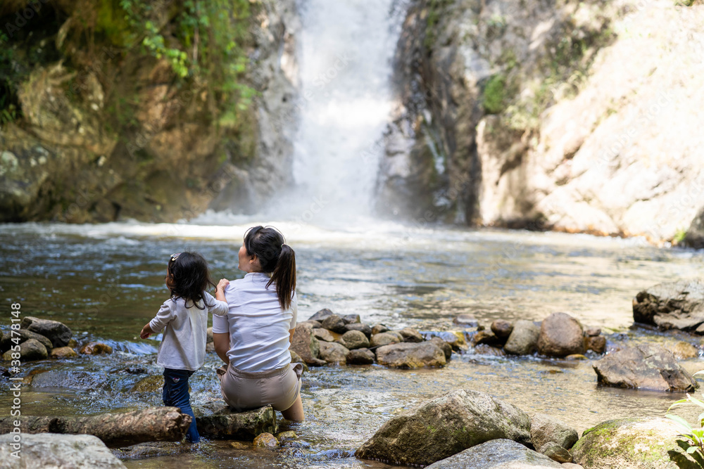 Mother and daughter sitting at the rocks against waterfall background. Mother and daughter sitting at the rocks against waterfall background.