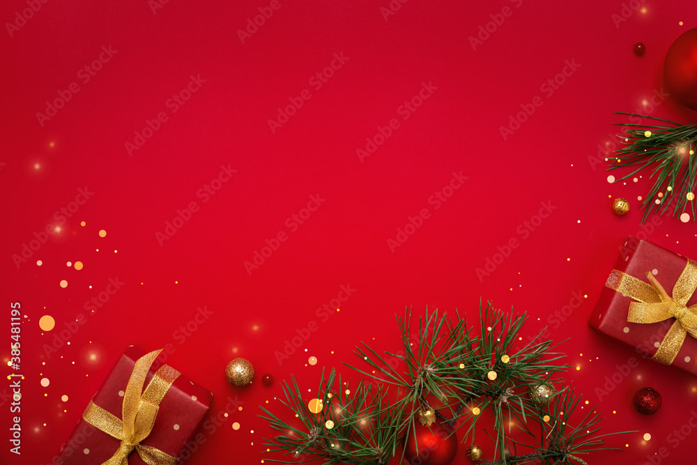 Christmas gifts, fir tree and gold decorations on red background. Copy space, flat lay.