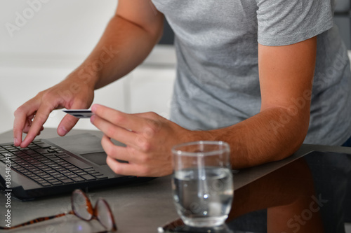 Close up of a male using a laptop and holding a credit card on an out of focus background. Online shopping and technology concept.