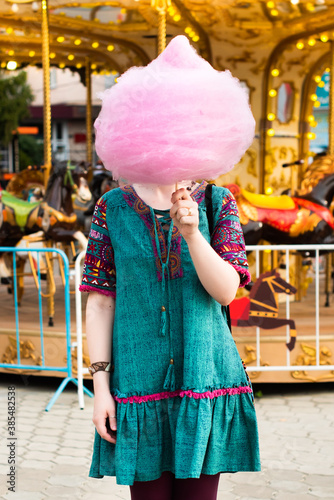 Young beautiful hipster woman eating cotton candy in an amusement park. girl covered her face with pink dessert. fun © Svetlana