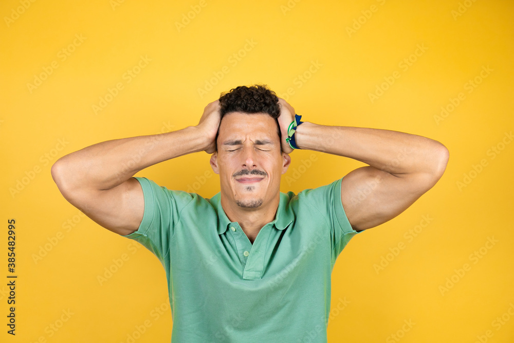 Young handsome man wearing green casual t-shirt over isolated yellow background suffering from headache desperate and stressed because pain and migraine with her hands on head Young handsome man wearing green casual t-shirt over isolated yellow background suffering from headache desperate and stressed because pain and migraine with her hands on head
