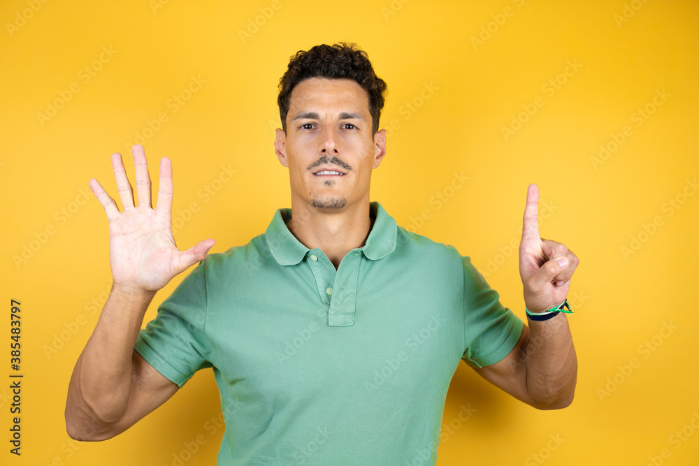 Young handsome man wearing green casual t-shirt over isolated yellow background showing and pointing up with fingers number six while smiling confident and happy Young handsome man wearing green casual t-shirt over isolated yellow background showing and pointing up with fingers number six while smiling confident and happy