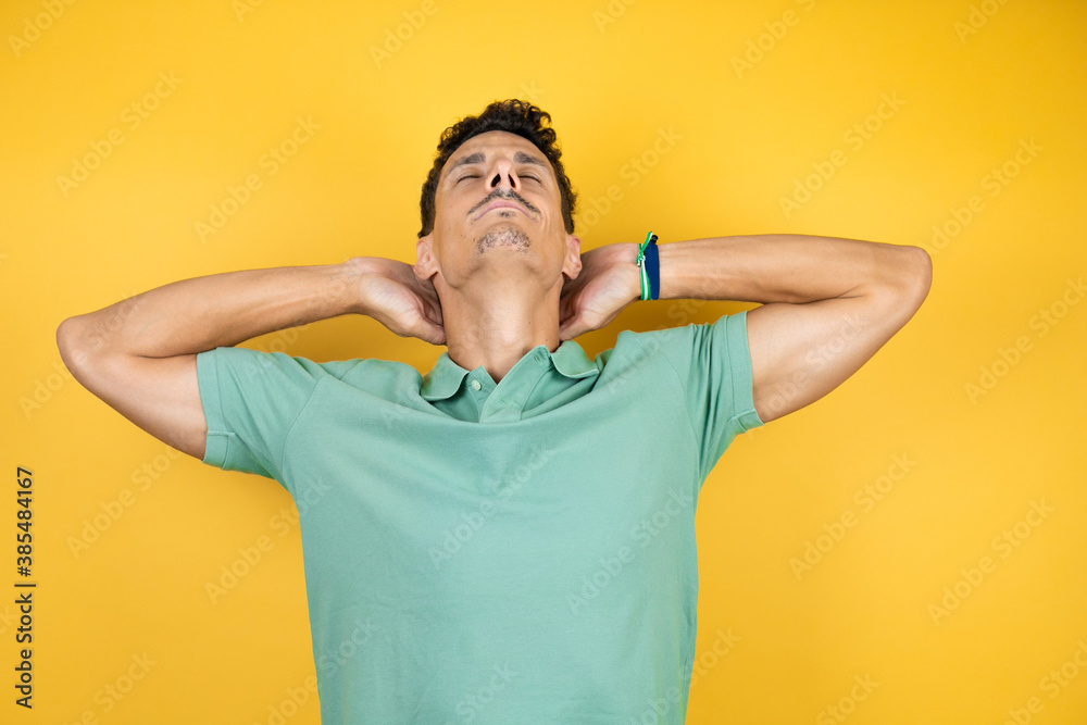 Young handsome man wearing green casual t-shirt over isolated yellow background relaxing and stretching, arms and hands behind head and neck smiling happy Young handsome man wearing green casual t-shirt over isolated yellow background relaxing and stretching, arms and hands behind head and neck smiling happy
