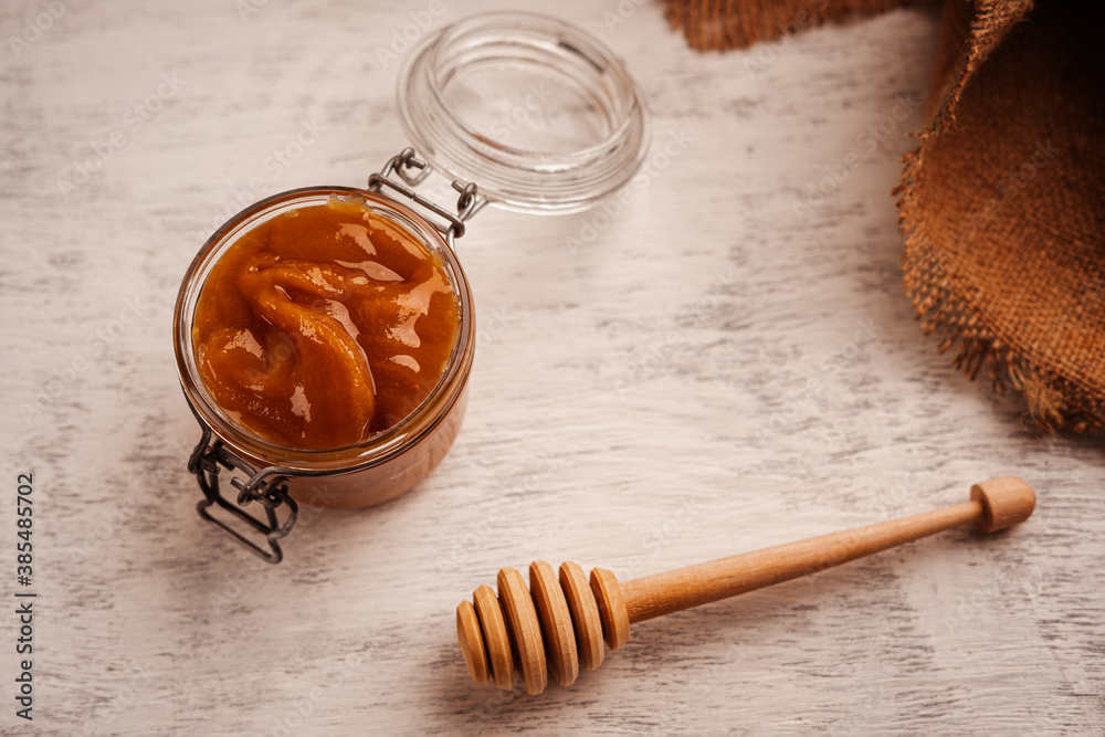 Brown thick honey in a glass jar near the Mace for honey and burlap top view Brown thick honey in a glass jar near the Mace for honey and burlap top view