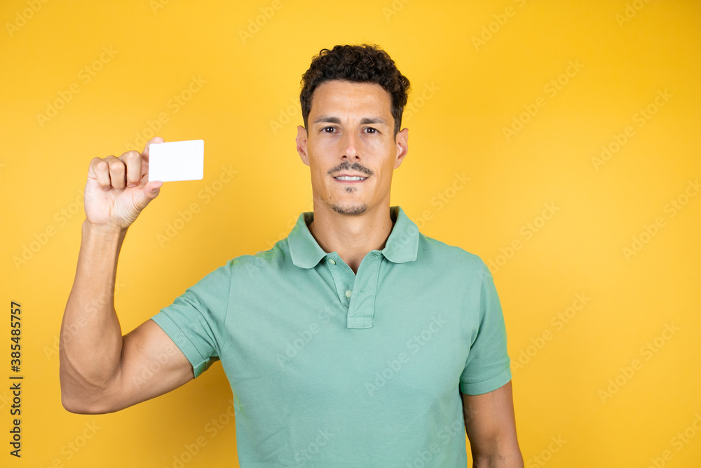 Young handsome man wearing green casual t-shirt over isolated yellow background smiling and holding white card