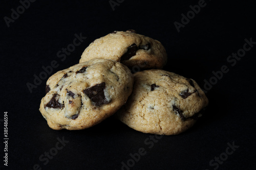 three fresh homemade American cookies with chocolate chips on black background