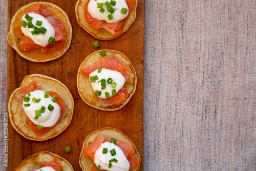 Homemade Blini with Smoked Salmon, Creme and Chives on a rustic wooden board, view from above. Space for text.