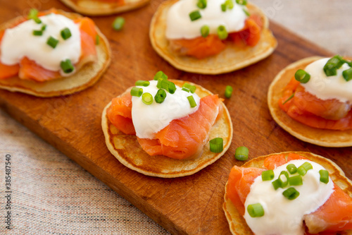 Homemade Blini with Smoked Salmon, Creme and Chives on a rustic wooden board, low angle view. Close-up.