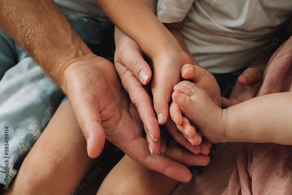 A close-up of the hands of all members of the family hold the feet of the newborn baby. A close-up of the hands of all members of the family hold the feet of the newborn baby.